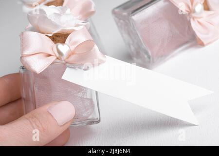 Rectangle strip white tag mockup with pink wedding favor with hand on white background, decorative bottle with gift tag mockup, element for packing. L Stock Photo