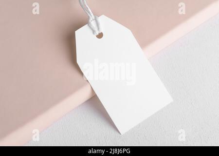 Rectangle white gift tag mockup with white cord, close up on beige and white background. Blank paper rectangular price tag mockup, Sale and Black Frid Stock Photo