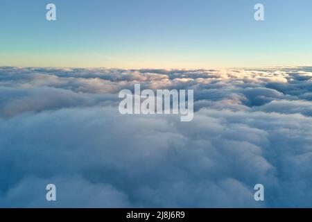 Aerial view from above at high altitude of dense puffy cumulus clouds flying in evening. Amazing sunset from airplane window point of view Stock Photo