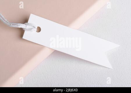 Rectangle strip white gift tag mockup with white cord, close up on beige and white background. Blank paper rectangular price tag mockup, Sale and Blac Stock Photo