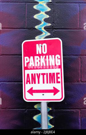 No parking anytime sign with colorful painted block wall in the background. Stock Photo