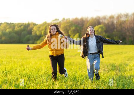 Mom and daughter casual dressed run in field at beautiful spring sunset. Mothers love concept. Stock Photo