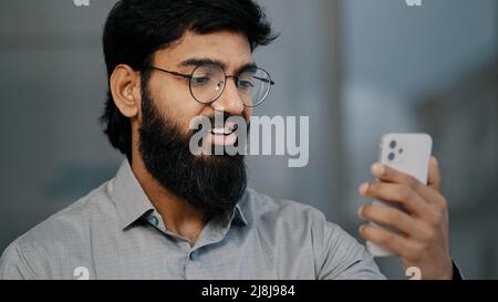 Arabian indian young bearded man businessman handsome entrepreneur hold smartphone talking online video communication with business partner virtual Stock Photo