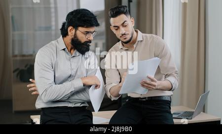 Multiracial business partners hispanic colleague consult male arabian co-worker team leader stand near desk discuss financial data analyze marketing Stock Photo