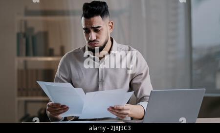 Frustrated hispanic young guy business man in office sadness accountant stressed about bank loan payments mistake in financial report document cross Stock Photo