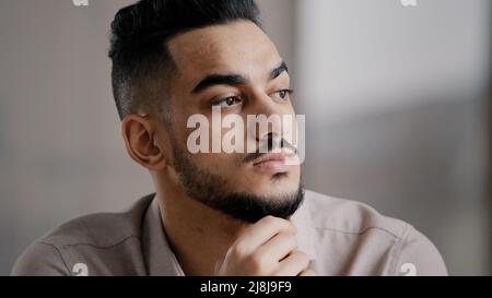 Pondering serious young arabian man businessman male student sit at home office hold hand on chin lost in thoughts dreamy looking away consider market Stock Photo