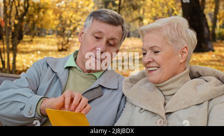 Smiling elderly couple aged partners grandparents senior wife husband open incoming postal envelope reads good news mail letter bank loan paper Stock Photo