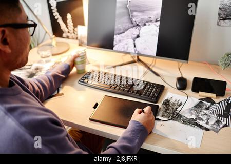 High angle portrait of male creator editing photographs at home office workplace and using pen tablet, copy space Stock Photo