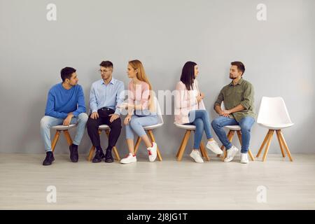 Smart young people sit in line for interviews and communicate with each other sharing experiences. Stock Photo