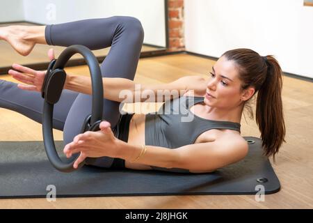 Young woman doing yoga leg stretch exercises using Pilates magic circle for resistance in a gym in a health and fitness concept Stock Photo