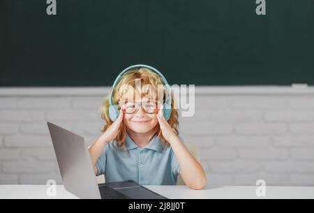 Clever school boy, cute pupil wears headphones writing on laptop, listen audio lesson use computer. Videocall, e-study with tutor distantly. Stock Photo
