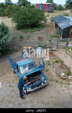 A senior male works on the engine of his old blue pickup truck, the hood lifted, shot from above, Lumberton, New Mexico, USA. Stock Photo