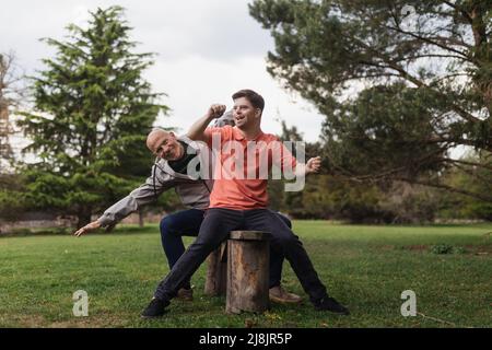 Happy senior father with his young son with Down syndrome sitting and having fun in park. Stock Photo