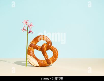 Bread bagel in heart shape with sesame seeds and pink hyacinth on sky blue background. Minimal food concept. Traditional Turkish pastry food. Stock Photo