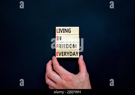 LIFE living in freedom everyday symbol. Concept words LIFE living in freedom everyday on blocks on black background. Businessman hand. Business LIFE l Stock Photo