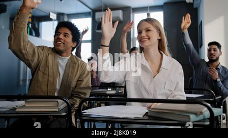 Diverse group smart students sitting in classroom at lesson carefully listening to teacher lecture studying at school or university all raising hands Stock Photo