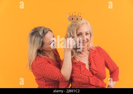 Happy loving older mature mother and grown millennial daughter laughing embracing, caring smiling young woman embracing happy senior middle aged mom having fun together, isolated, orange background. High quality photo Stock Photo