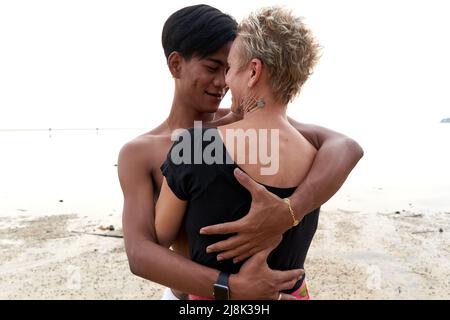 Lovers gazing tenderly at each other while embracing on a beach at sunset Stock Photo