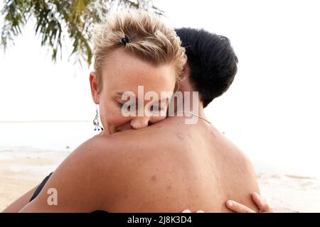 Caucasian adult woman embracing her asian couple in a beach Stock Photo