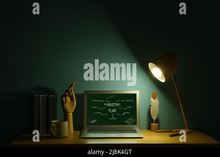 Modern laptop with components of marketing plan on screen in dark office Stock Photo