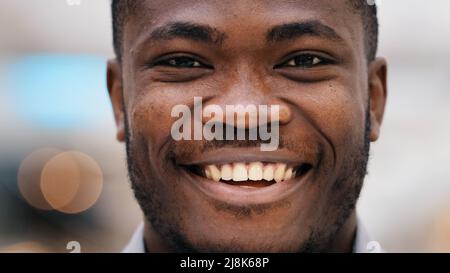 Close-up portrait young confident happy african american male client raises eyes looking at camera smiling white healthy toothy dental smile happy Stock Photo