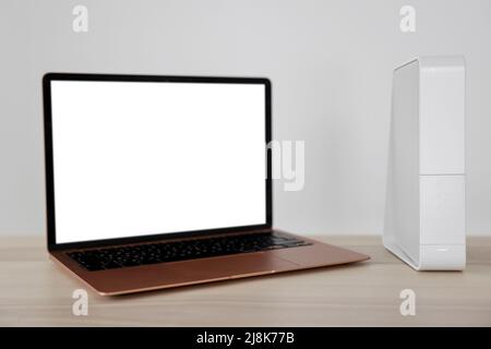 Modern laptop and wi-fi router on table near white wall Stock Photo