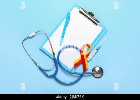 Awareness ribbon with stethoscope, syringe, pen and clipboard on blue background. Hepatitis concept Stock Photo