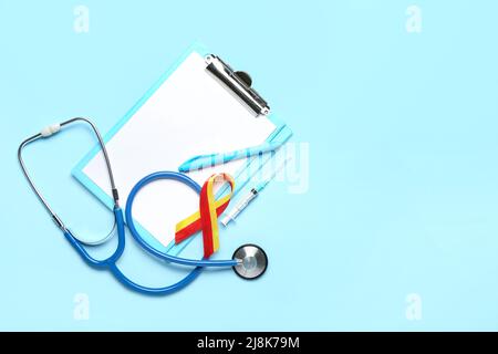 Awareness ribbon with stethoscope, syringe, pen and clipboard on blue background. Hepatitis concept Stock Photo