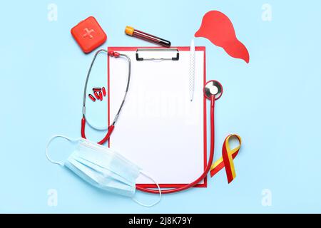 Awareness ribbon with clipboard, pills, paper liver, medical mask and stethoscope on blue background. Hepatitis concept Stock Photo