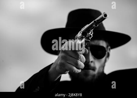 Cowboy shooter in black suit and cowboy hat. Serious man with wild west guns, retro pistol revolver and marshal ammunition. American western Sheriff Stock Photo