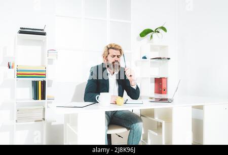 Bearded young businessman working at modern office. Office worker making notes on the documents. Elegant business man analyzing data in office. Stock Photo