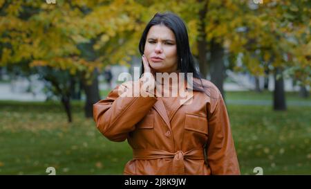 Young hispanic woman standing outdoors feeling toothache holding hand on cheek jaw has dental problems suffering from pain unpleasant symptoms needs Stock Photo