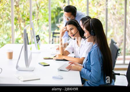 Team of diverse hotline operators with headphones providing service to clients at call center. Stock Photo