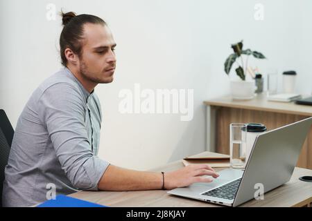 Serious young entrepreneur with man bun checking e-mails on laptop Stock Photo