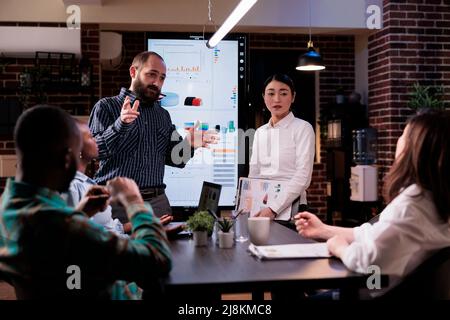 Diverse multiethnic business people analyzing management strategy working overtime in company office meeting room late at night. Sales team discussing marketing strategy in startup workspace. Stock Photo