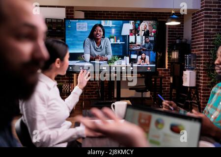 Confused startup coworkers talking during online video conference in late night meeting feeling tired doing overtime. Mixed team talking about sales with remote coworkers over internet call. Stock Photo