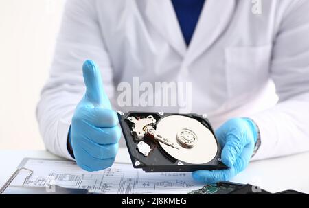 Man in uniform hold disassembled hard drive from computer, hdd and reader, show thumbs up Stock Photo