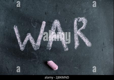 War. A word is written in pink chalk on a black chalkboard. Handwritten text. A piece of colored chalk hangs next to it. Stock Photo