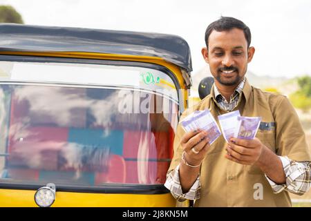 Happy smiling auto Rickshaw driver counting money while standing next to auto - concept of successful business, financial, banking and self employment Stock Photo