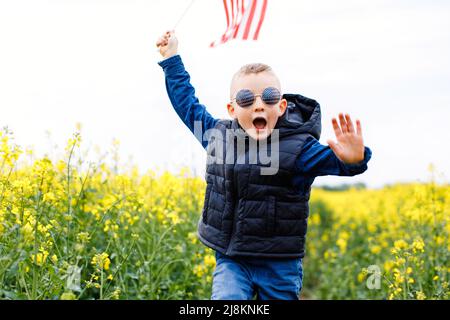 Happy little boy patriot running in the field with American flag. USA celebrate 4th of July Stock Photo