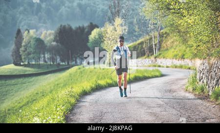 A young man while practicing Nordic walking with poles on a hill road Stock Photo