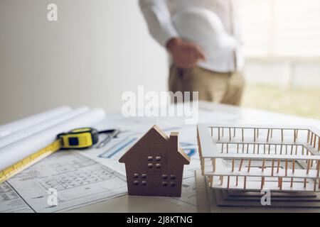 Engineer is holding a helmet standing in his office and has a blueprint and model on his desk. Stock Photo