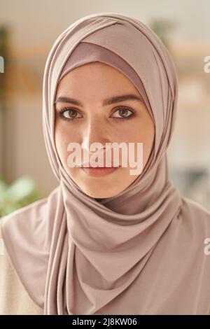 Vertical head and shoulders close-up portrait shot of attractive Muslim woman wearing pale pink hijab looking at camera Stock Photo