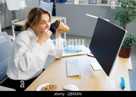 Busy business woman drinking coffee with cookies while working on computer Stock Photo