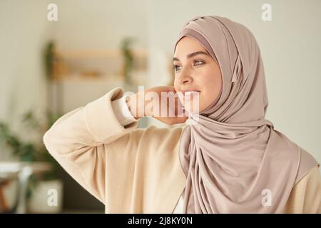 Beautiful young Muslim female model fixing her hijab and looking away, horizontal chest up portrait shot Stock Photo