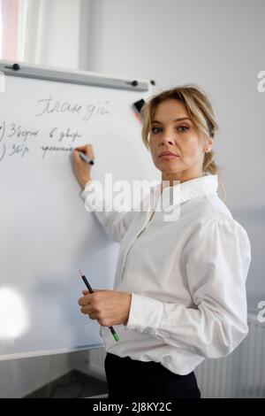 Portrait of a serious business woman writing on a magnetic whiteboard during a presentation in the office Stock Photo