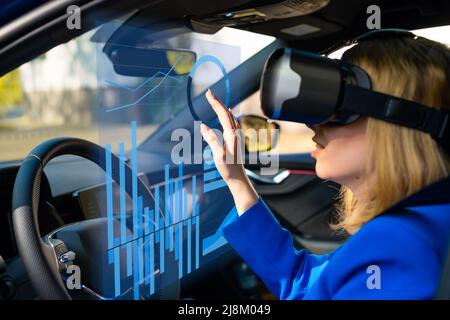 Digitally generated graphics and charts interface managed by business woman in vr googles sitting in the car in a blue suit. Metaverse cyber world technology concept.  Stock Photo