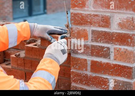 Bricklayer laying bricks on mortar on new residential house construction. Get construction qualification Stock Photo