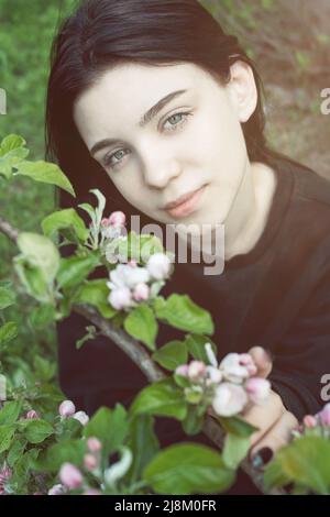 Pretty  teen girl are posing in garden near blossom apple tree with pink flowers. Spring time Stock Photo