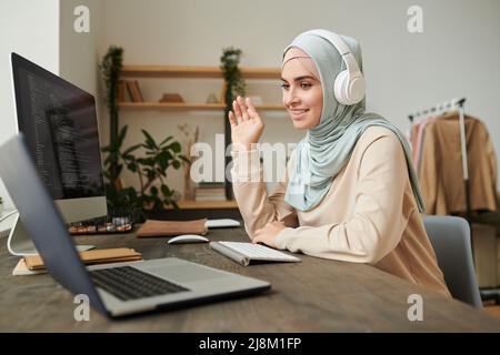 Middle Eastern professional programmer wearing hijab and headphones taking part in online meeting Stock Photo